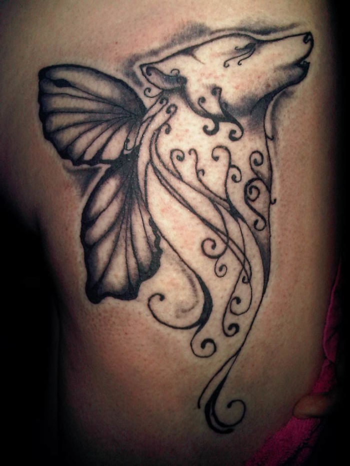 Artistic dog tattoo with intricate swirls and butterfly wings on skin.