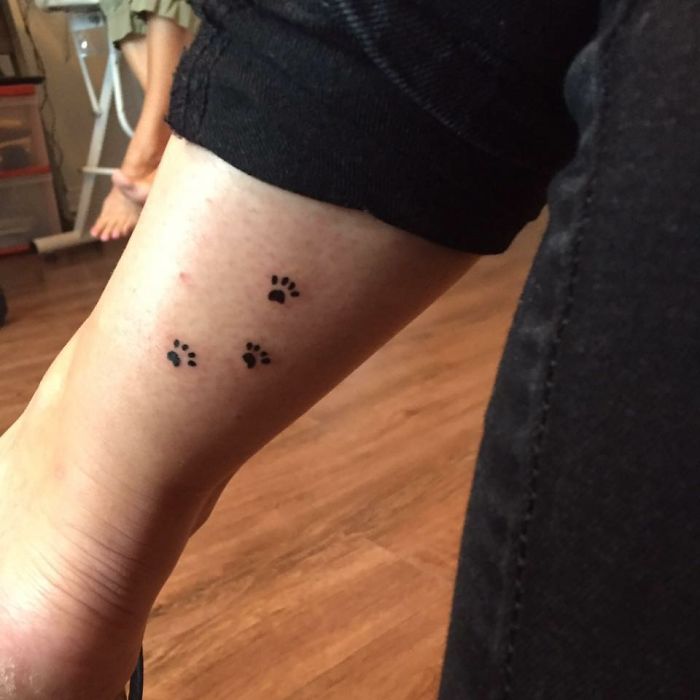 Small dog paw prints tattoo on ankle, minimalistic design on leg, showcasing unique dog tattoo idea.
