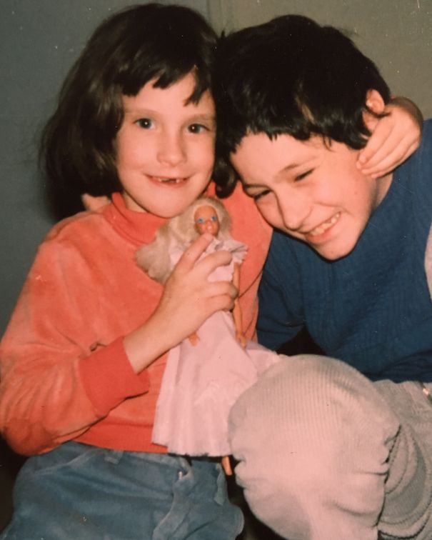 Two kids smiling, with one holding a doll, showcasing their own haircut experiment and playful spirit.