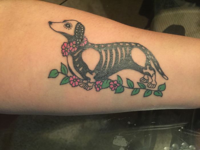 Dog tattoo idea featuring a skeleton design with floral accents on an arm.