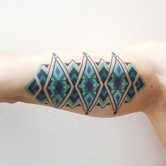 Amazonian tribal art tattoo by Brazilian artist Brian Gomes on an arm, featuring geometric shapes in green and blue.