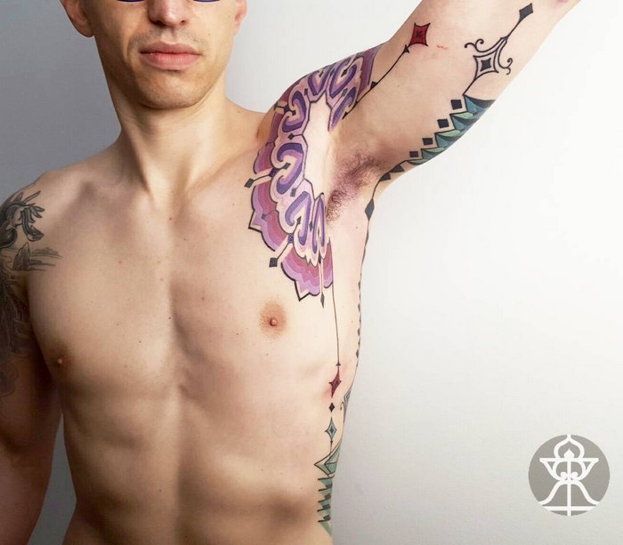 Man with intricate Amazonian tribal tattoo by Brazilian artist on arm and chest, showcasing vibrant colors and patterns.