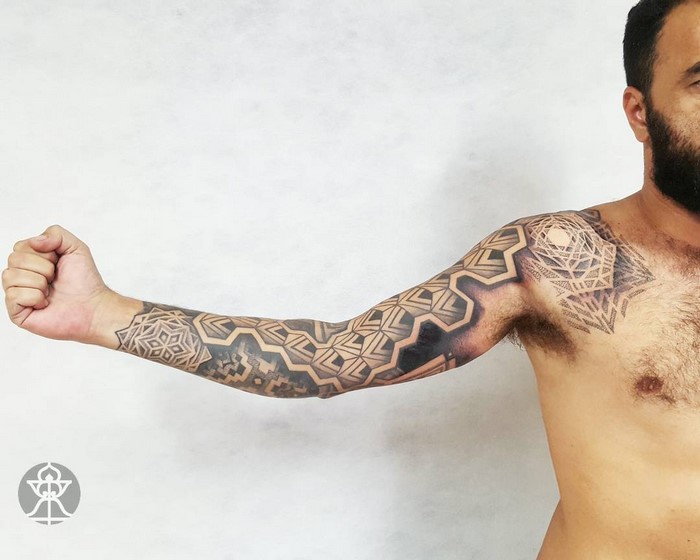 A man displays an arm tattoo inspired by Amazonian tribal art, featuring geometric patterns by artist Brian Gomes.