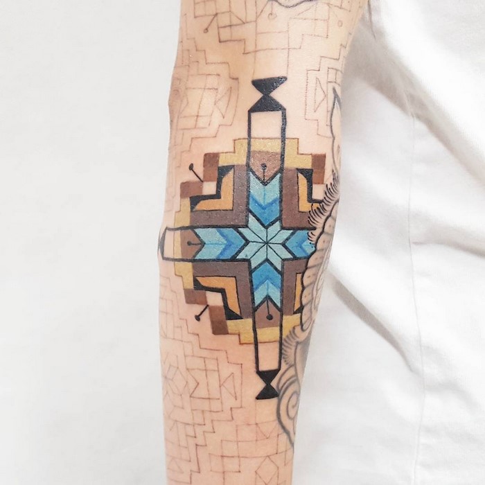 Arm tattoo featuring Amazonian tribal art in blue and brown design by Brazilian artist.