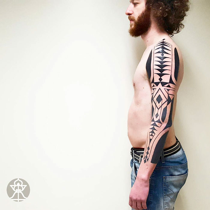 Man with Amazonian tribal art tattoo on arm by Brazilian artist Brian Gomes, showcasing intricate black geometric patterns.