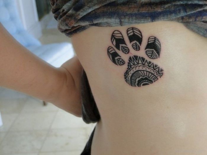 Intricate dog paw tattoo with geometric patterns on a person's rib cage.
