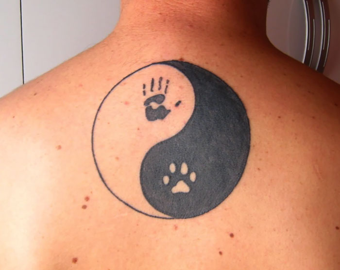 Yin-yang tattoo on back featuring dog paw and human handprint, symbolizing balance.