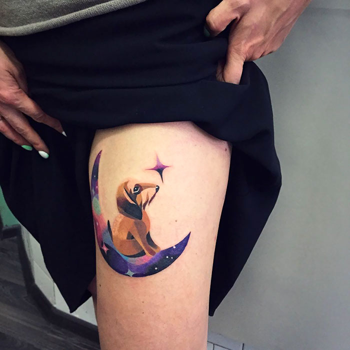 Colorful dog tattoo with crescent moon design on thigh, featuring vibrant space-themed elements.