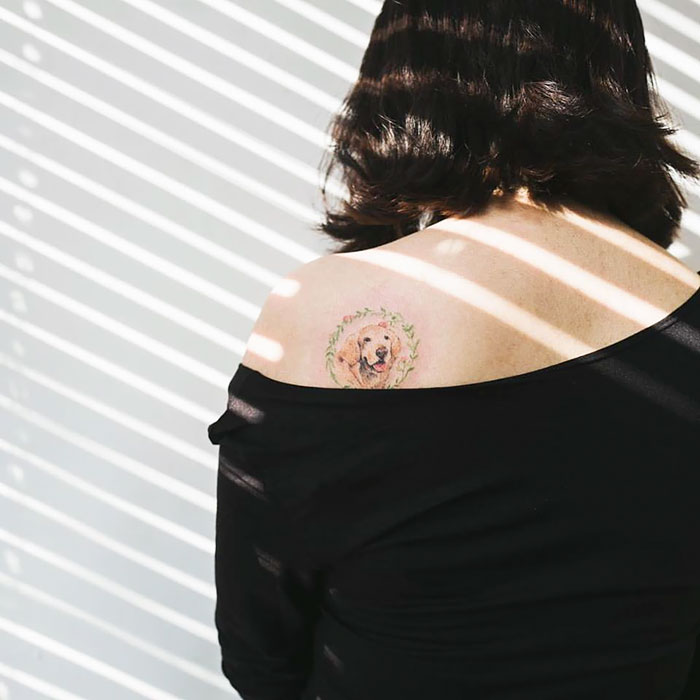 Dog tattoo on woman's shoulder, surrounded by floral design, illuminated by striped light.
