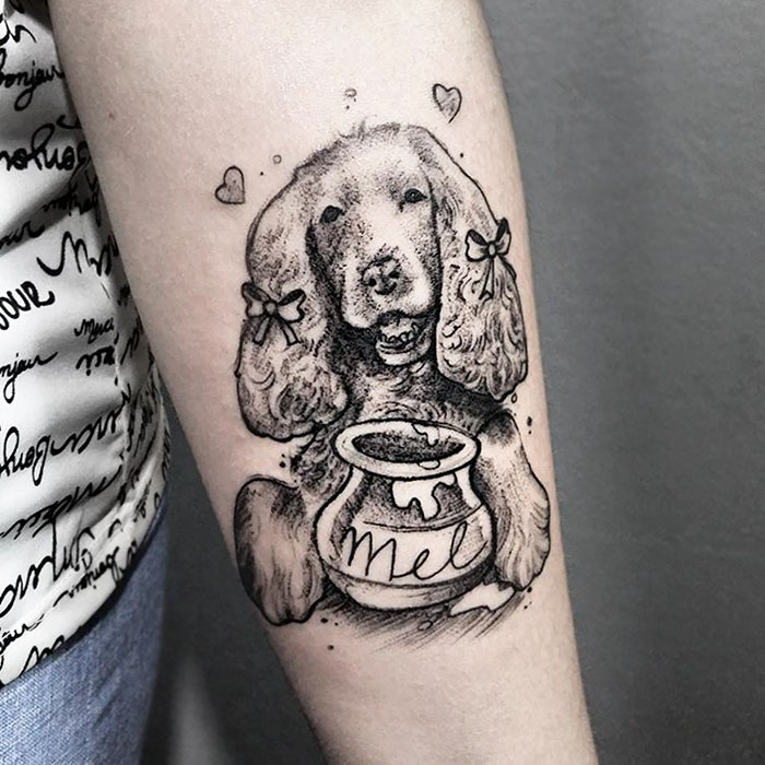 Dog tattoo on arm featuring a cute dog with bows and a honey pot labeled "mel".