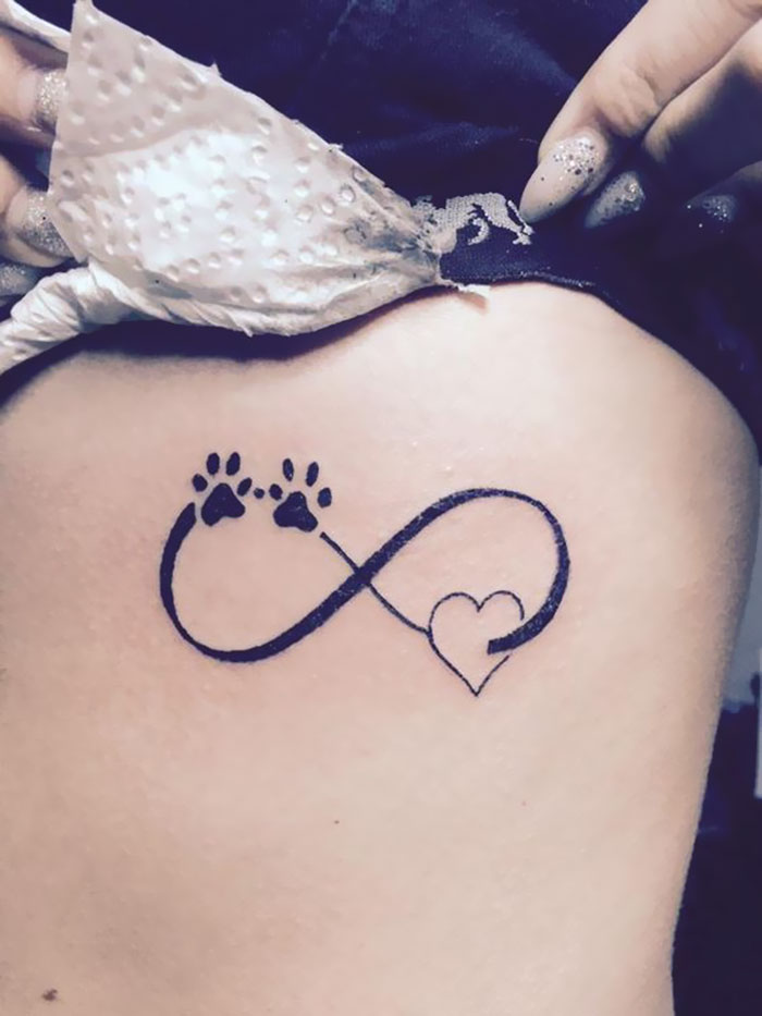 Dog tattoo with paw prints and heart forming an infinity symbol.