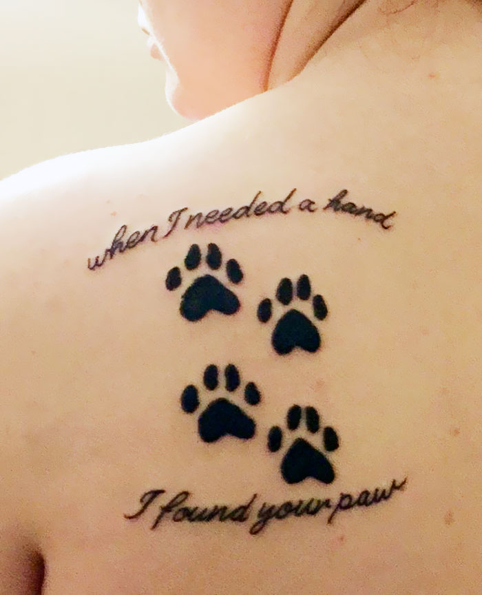 Dog tattoo featuring paw prints and the quote "when I needed a hand, I found your paw" on a person's shoulder.