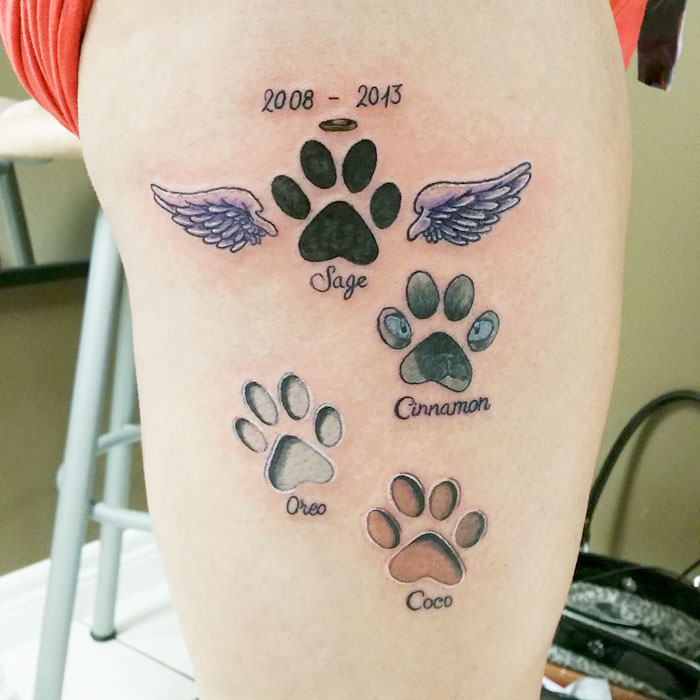 Dog tattoo featuring paw prints with names Sage, Cinnamon, Oreo, and Coco, including wings and dates.