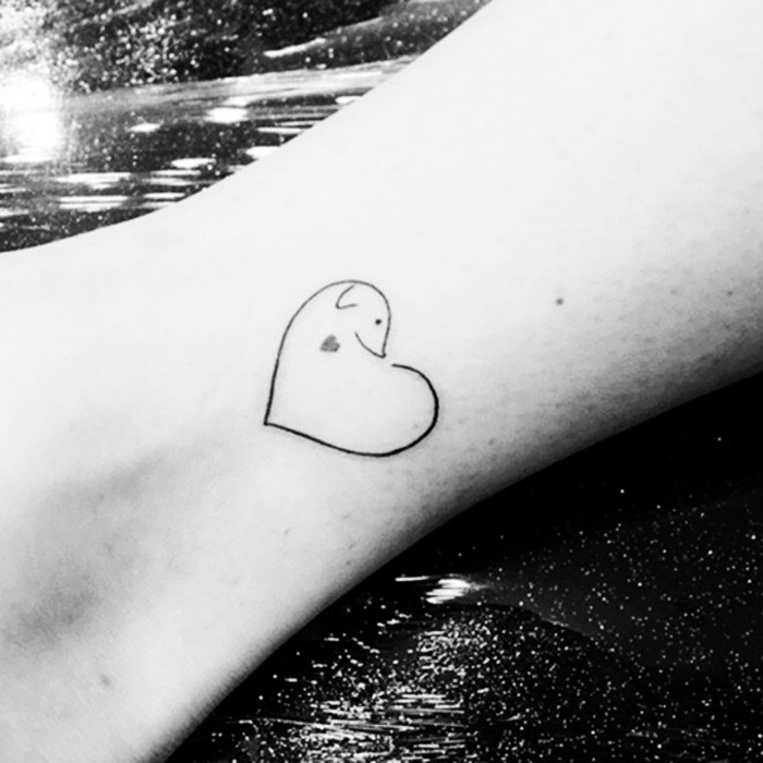 Minimalistic dog tattoo in heart shape on ankle, showcasing creative dog tattoo ideas.