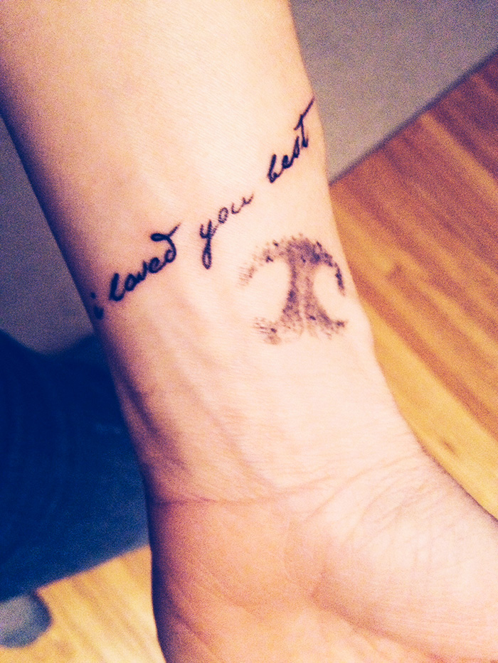 Dog tattoo with a paw print and cursive script on a wrist.