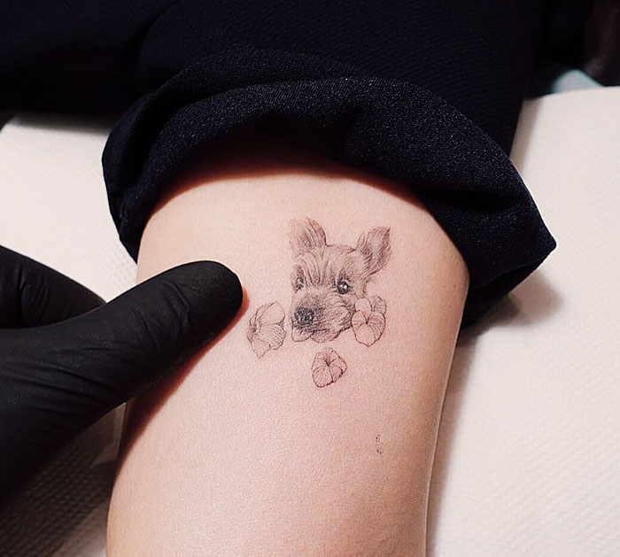 Dog tattoo on a person's arm, depicting a realistic puppy face with paws, being admired by a gloved hand.