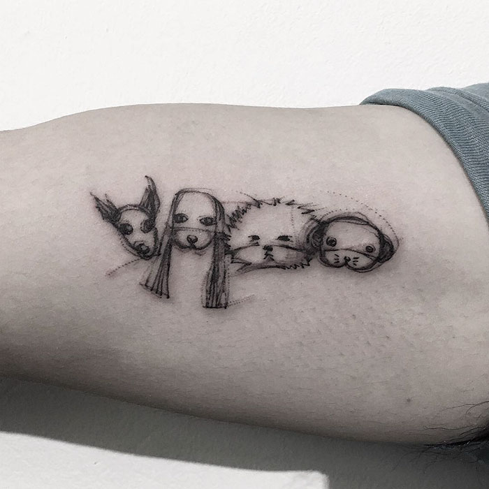 Minimalist dog tattoo art featuring four dog faces in a row on a forearm.