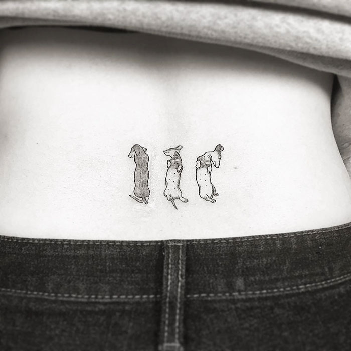 Minimalist dog tattoo depicting three small dogs on a person's lower back.