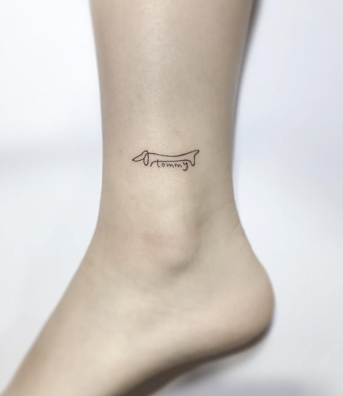 Minimalist dog tattoo on ankle, featuring an outline of a dachshund and the name "Tommy."