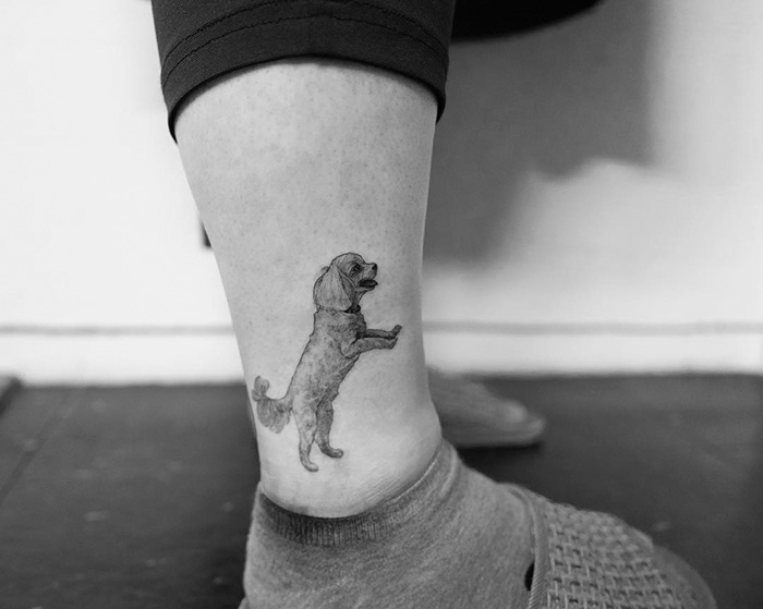 Ankle with small, detailed dog tattoo in black and white, showcasing one of the best dog tattoo ideas.