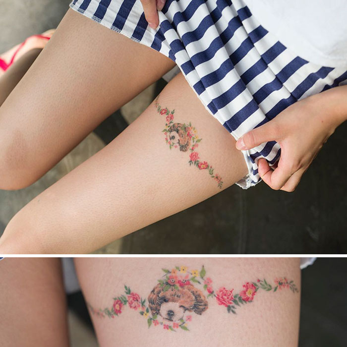 Dog tattoo on thigh with floral design, showcasing adorable puppy portrait surrounded by colorful flowers.