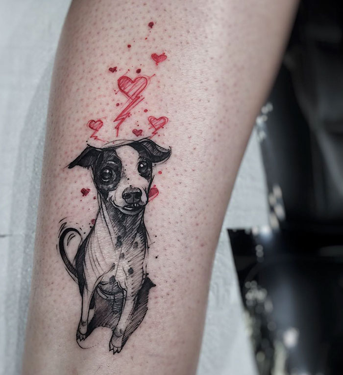 Dog tattoo featuring a black and white pup with red hearts and lightning bolt accents on skin.