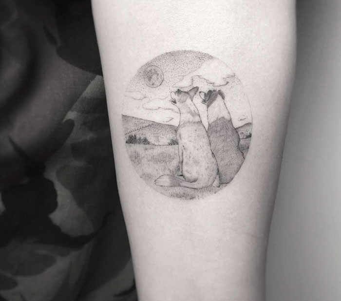 Dog tattoo of two dogs sitting together, looking at the sky with scenery in the background.