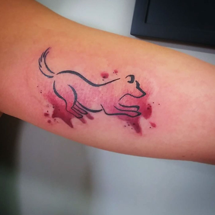 Minimalistic dog tattoo design with splattered red ink on forearm.