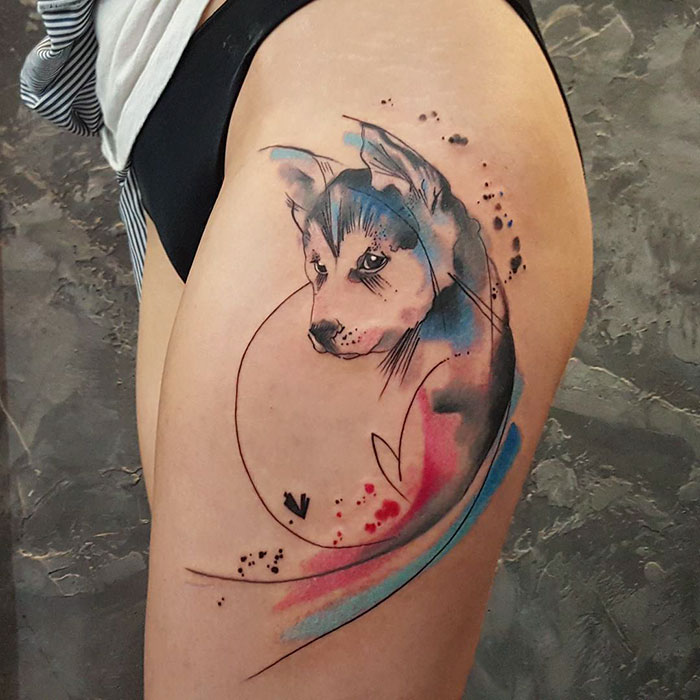 Watercolor dog tattoo on thigh with abstract blue and red splashes.