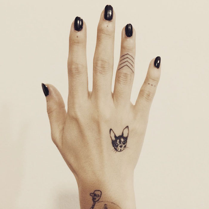 Hand displaying a small dog tattoo, showcasing one of the best dog tattoo ideas, with black nail polish.
