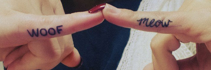 Fingers with "woof" and "meow" tattoos touch, showcasing creative dog tattoo ideas.