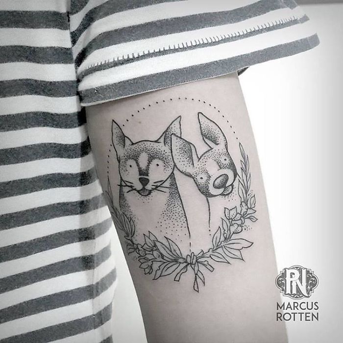 Two dog tattoo designs on arm with floral details.
