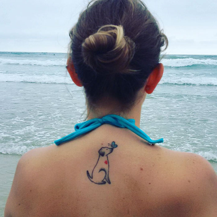 A simple dog tattoo on a woman's back at the beach.