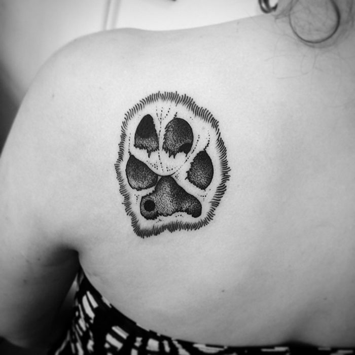 Black and white dog paw tattoo on a person's shoulder, showing intricate detailing and texture.