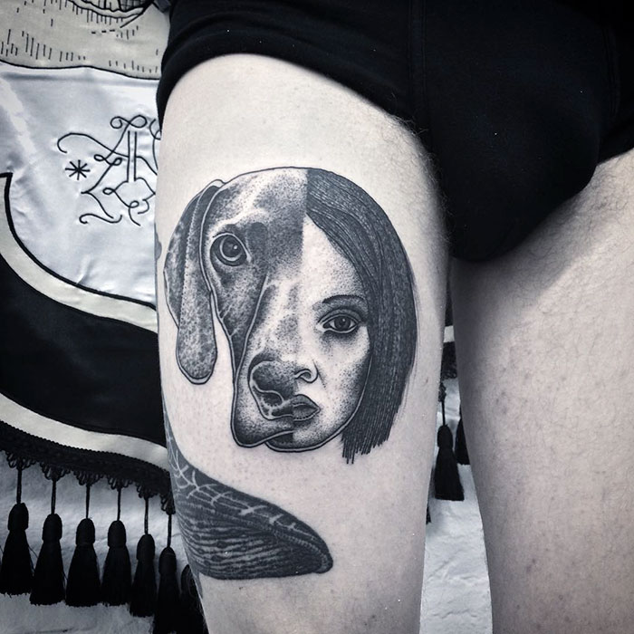Unique dog tattoo blending canine and human face on thigh.