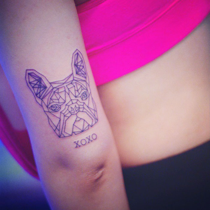 Geometric dog tattoo with "XOXO" on an arm, featuring bold lines and modern design.