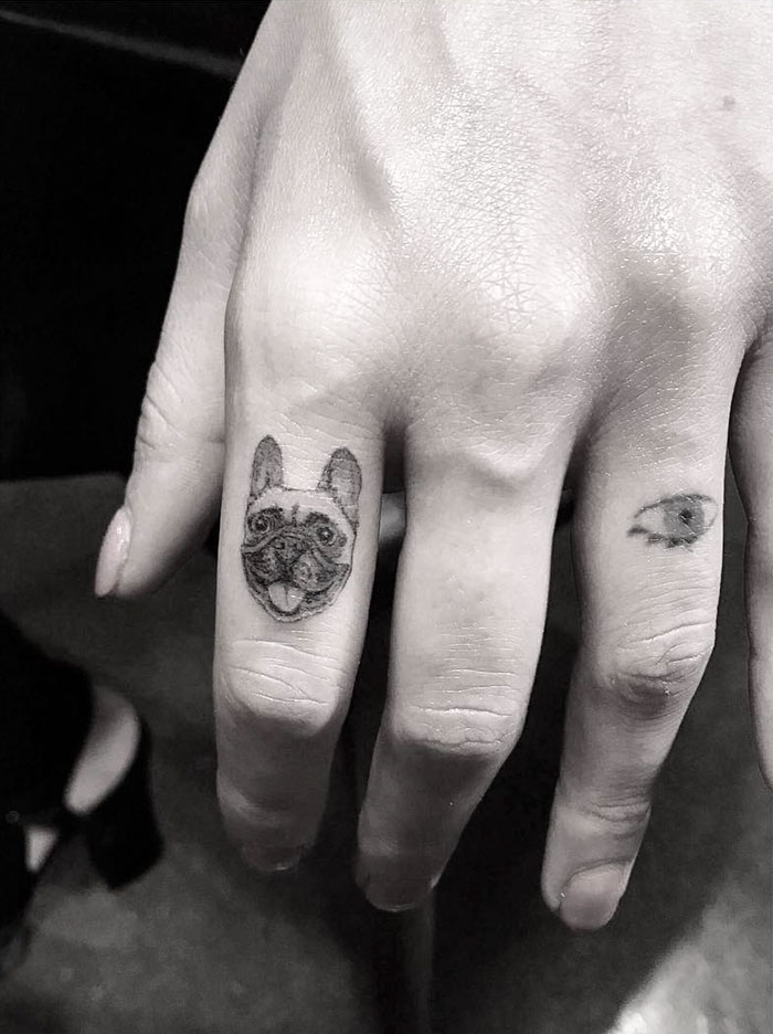 Dog tattoo on finger with a small eye tattoo on another finger, showcasing creative canine ink art.