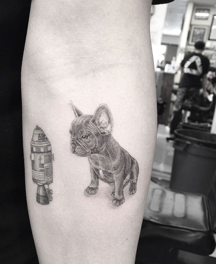 Detailed dog tattoo with a small rocket on the forearm, showcasing creative pet art.