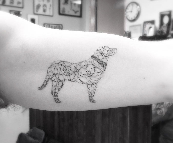 Minimalist dog tattoo design on inner arm, featuring delicate line patterns.