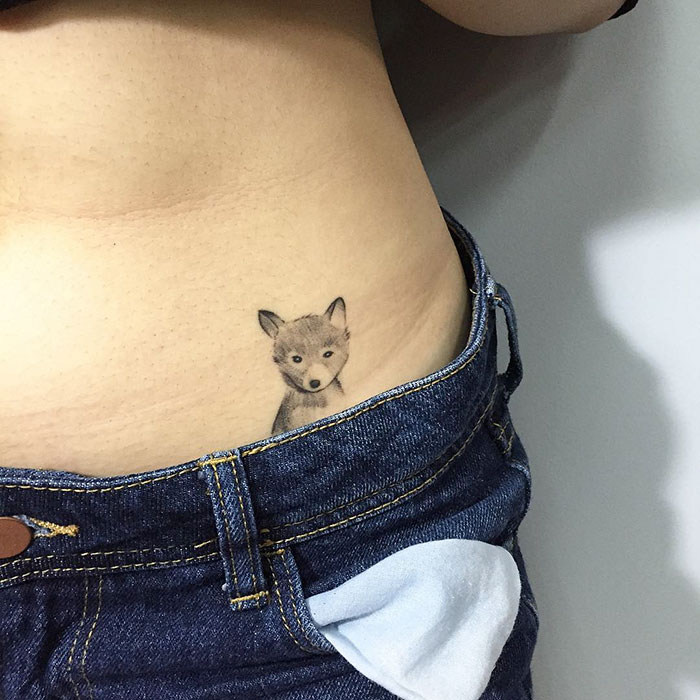 Dog tattoo on waistline, peeking from jeans, showcasing unique and creative design.