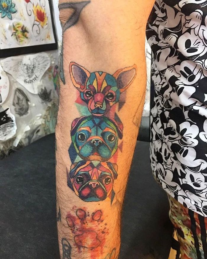 Colorful dog tattoo on forearm featuring three geometric canine designs in vibrant hues.