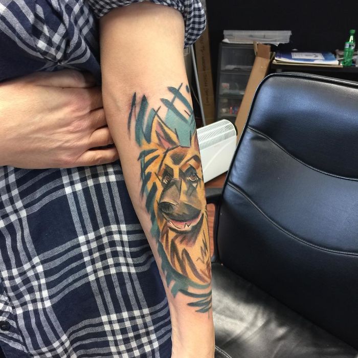 Colorful dog tattoo on forearm showcasing unique art style in cozy office setting.