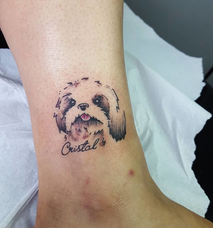 Dog tattoo on ankle featuring a fluffy pup with the name "Cristal" beneath it.