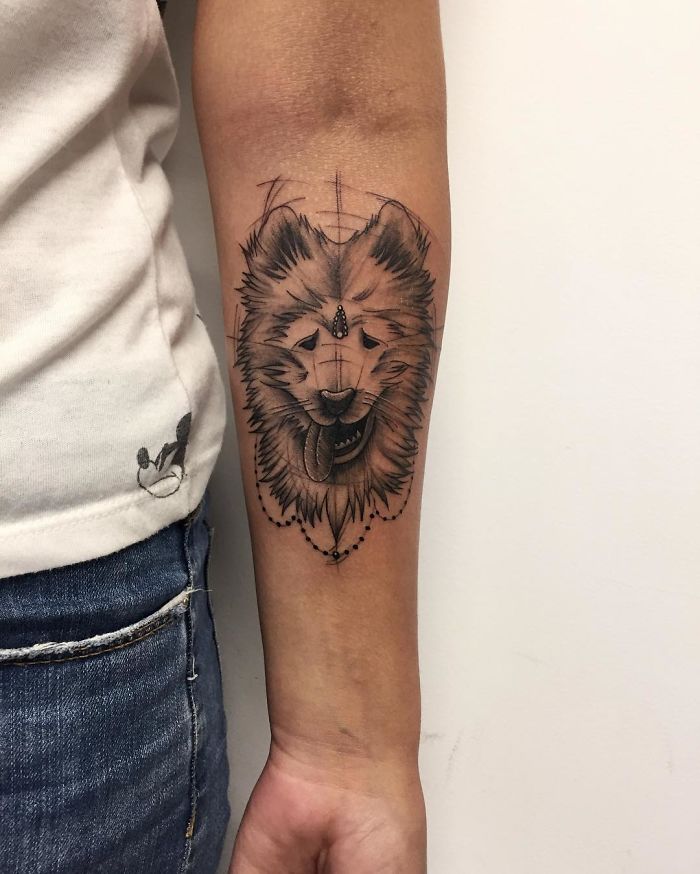 Dog tattoo design on forearm featuring detailed sketch of a fluffy dog head in black and grey ink.