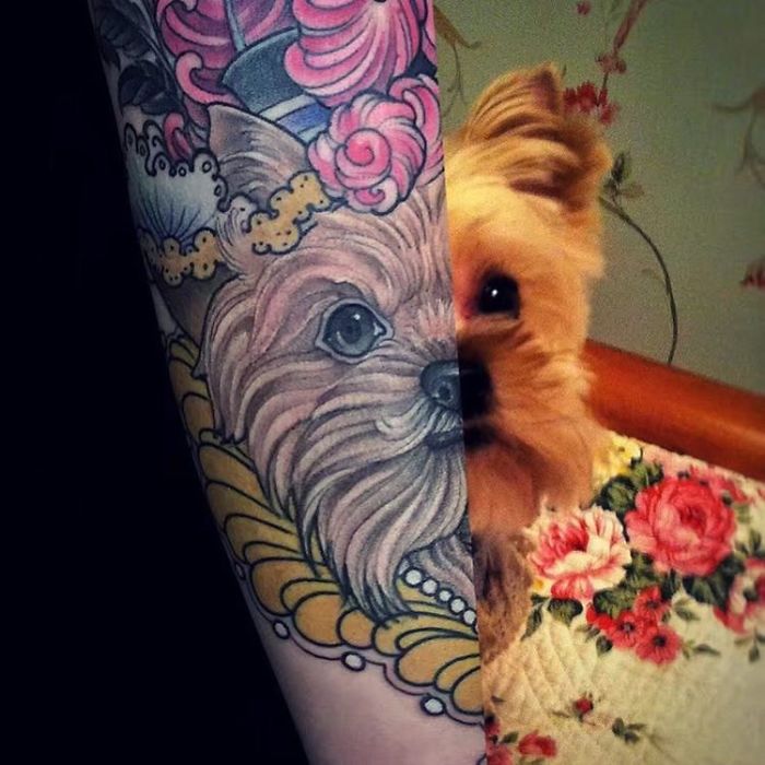 Dog tattoo on arm with floral design, next to a real dog peeking from behind.