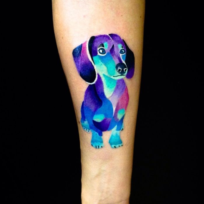 Colorful dog tattoo design on forearm, featuring a stylized dachshund in vibrant blues and purples.