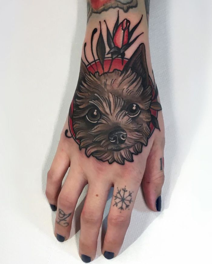 Dog tattoo on hand with floral accents, showcasing intricate details and shading.
