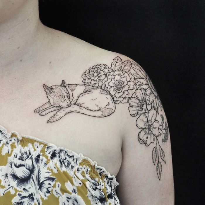 Intricate dog tattoo design featuring a sleeping dog among flowers on a person's shoulder.