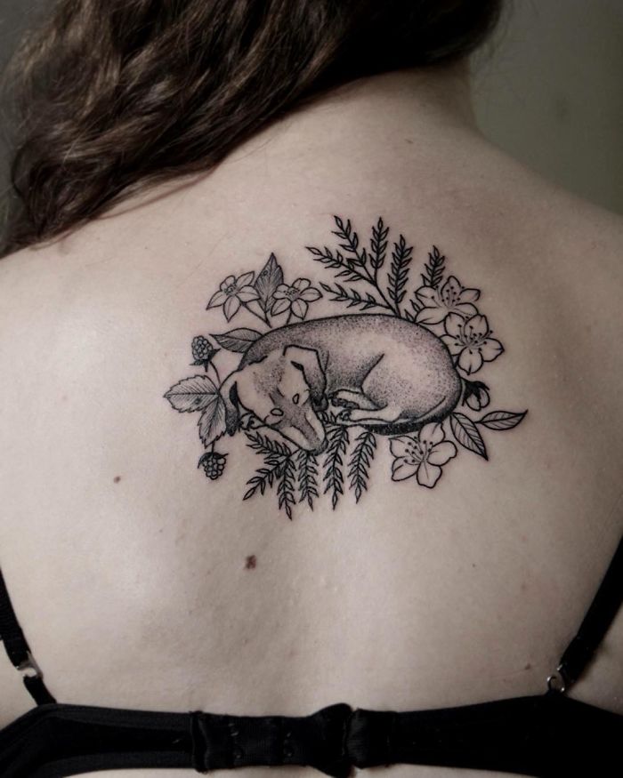 Dog tattoo on back featuring a resting dog surrounded by flowers and leaves.