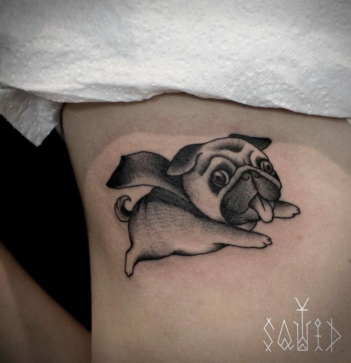Dog tattoo of a playful pug with a cape on a person's skin, showcasing a cute and whimsical design.